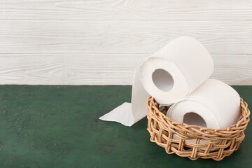 Wicker bowl with rolls of toilet paper on green table