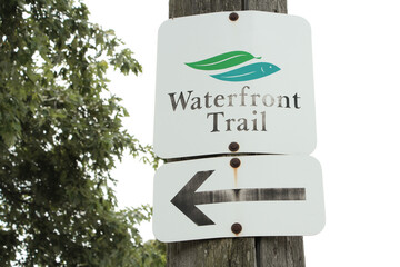 waterfront trail sign on wood post with arrow sign below pointing left with sky behind, square and...
