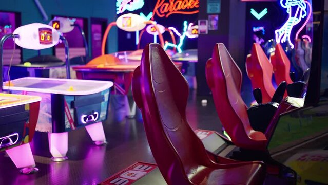 Row of racing arcade machines inside a neon-lit shopping mall, complemented by various gaming machines in an illuminated arcade. Entertainment concept.