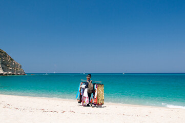 Fototapeta na wymiar Fliegender Händler am Strand von Tropea bietet seine Waren an