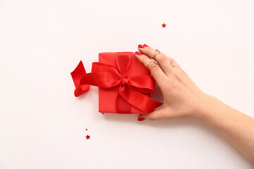 Female hand with stylish red manicure holding gift box on white background