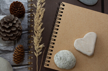 Notebooks, cones, stones on a wooden table top view. Workspace, artist's creative workshop. Cozy home interior in brown tones.