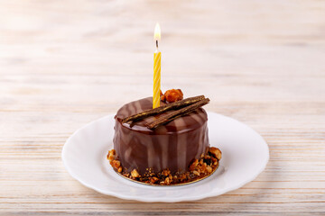 Fresh delicious chocolate cake with candle on plate on white wooden background. Caramel glaze and decoration add appeal and desire