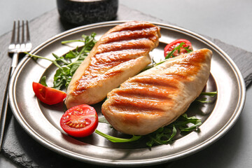 Plate of tasty grilled chicken breast with arugula and tomatoes on grey background