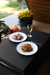 there is food on the rattan table. Pilaf and Greek vegetable salad and a glass of white wine on the table. Eat dinner outside. Garden furniture for home. rattan furniture on the terrace