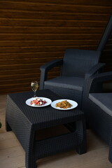 there is food on the rattan table. Pilaf and Greek vegetable salad and a glass of white wine on the table. Eat dinner outside. Garden furniture for home. rattan furniture on the terrace