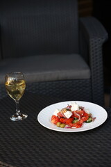 there is food on the rattan table. Greek vegetable salad and a glass of white wine on the table. Eat dinner outside. Garden furniture for home. rattan furniture on the terrace