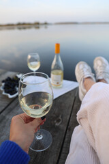 picnic by the lake with white wine, grapes, cheese. aesthetic picnic for girls. a woman takes a glass of white wine with her hand. Picnic at the wooden pier by the lake 