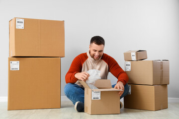 Young man unpacking parcel near light wall