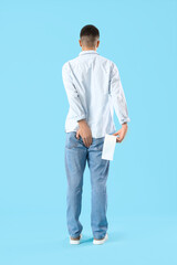 Young man with hemorrhoids and toilet paper on blue background, back view