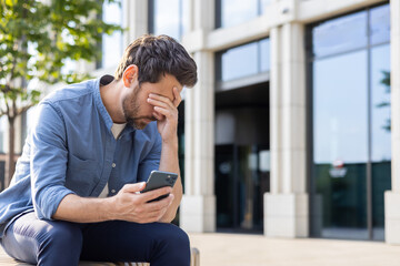Stressed businessman in casual attire outside corporate building holding head