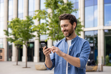 Smiling bearded businessman using smartphone in urban setting with office background