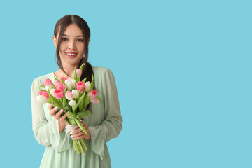 Pretty young Asian woman with bouquet of beautiful tulips on blue background. International Women's Day