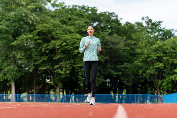 Happy asian slim woman wearing sportswear jogging on track at sport stadium. Young beautiful asian female in sports bra running outdoor. Workout exercise in the morning. Healthy and active lifestyle