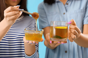 Young women with glass cup of tea and honey on blue background, closeup