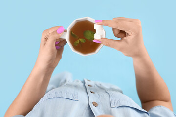 Young woman with sugar and cup of mint tea on blue background, top view