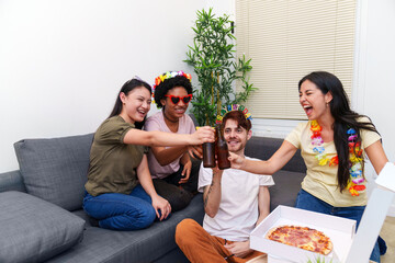Excited friends clinking beer bottles and enjoying pizza, celebrating a special birthday in the comfortable setting of their home.