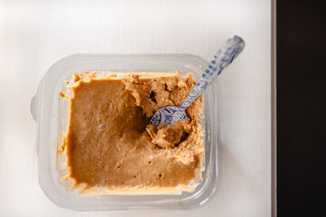 A clear plastic tub of peanut butter with a patterned blue spoon.