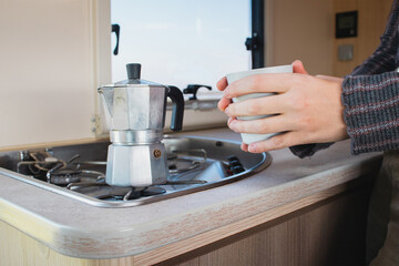 hands hold a glass next to a coffee pot in a coach kitchen.