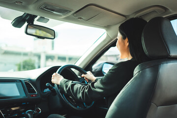 Young beautiful asian business women in suit getting new car. She very happy and excited. Smiling female driving vehicle on the road on a bright day.