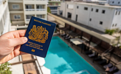 Man holding UK passport against the backdrop of a luxury hotel.