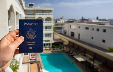 Man holding USA passport against the backdrop of a luxury hotel.