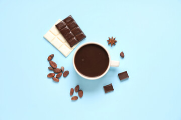 Cup of tasty hot chocolate with cocoa beans on blue background