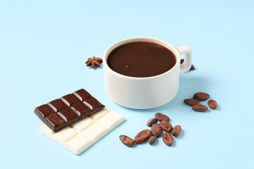 Cup of tasty hot chocolate with cocoa beans on blue background