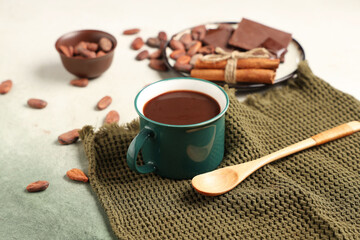 Cup of tasty hot chocolate with cocoa beans, cinnamon and napkin on green grunge background