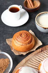 Buns with cream, cinnamon sticks and cup of coffee on black grunge background