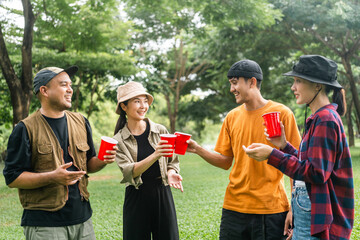 Cheers! Group of asian people friend party camping in nature making toasting with soft drink and beer red cup. Hangout party outdoor in campsite nature forest background on holiday weekend vacation
