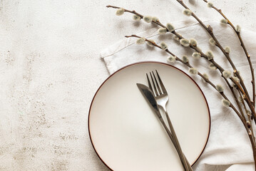 Easter table setting with empty white ceramic plate with cutlery  and spring willow branches on...