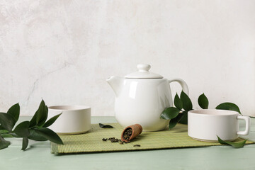 Bamboo with cups of tea, teapot and spoon with dry leaves on green background