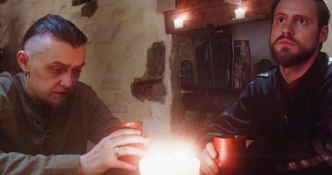 Guys friends drink ale together in tavern. Bored men in medieval clothes rest sitting at table in old pub. Upset guests with alcohol beverages at inn
