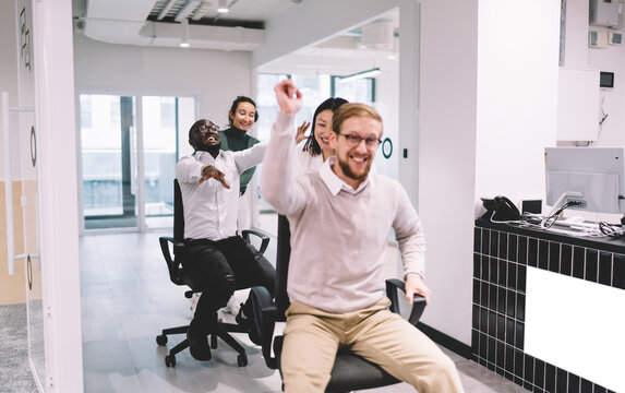 Cheerful multiethnic employees rolling colleagues on chairs - Powered by Adobe