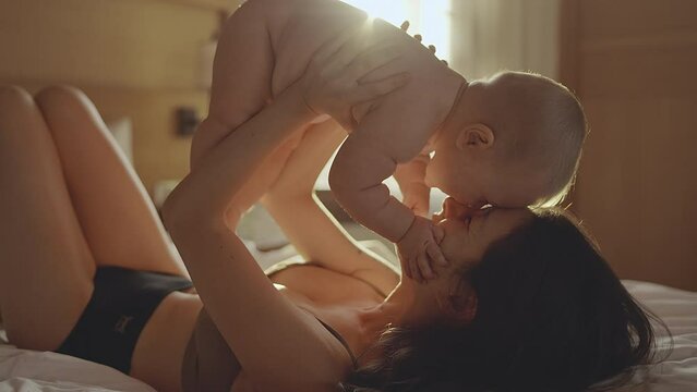 Mother and her Newborn Baby. Happy Mom holding her New born child boy kissing and hugging. Cinematic sunset light. Unconditional Love. Maternity concept. Parenthood. Motherhood. Beautiful Happy Family