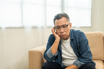 Asian mature old man sitting bored serious thinking in living room at home. Portrait of serious depressed senior asian man. Mature People with problem in life