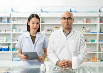 Fototapeta na wymiar Two asian man and woman professional Pharmacist colleagues working at drugstore pharmacy. Asking the questions of medication standing near pharmacy shelves counter with medicines