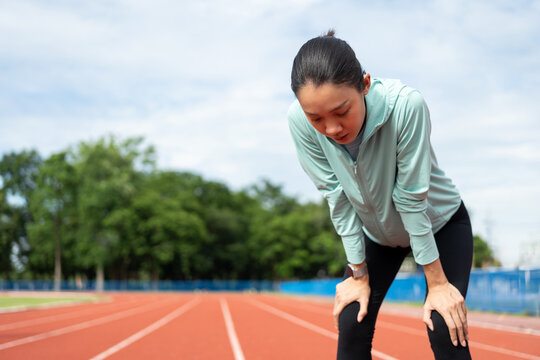 Beautiful woman tired during jogging on running track. Young asian female intense training workout challenge breathing exhausted. Exercise in the morning. Healthy and active lifestyle concept.