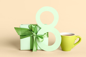Figure 8 made of paper with gift box and cup of tea on beige background. International Women's Day