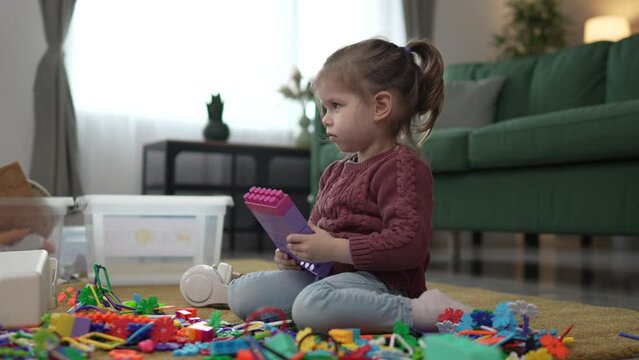 One girl caucasian toddler play on the floor at home with brick blocks