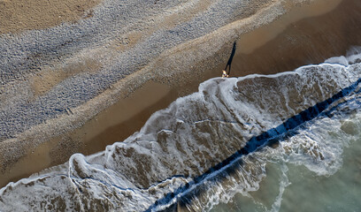 Aerial drone point of view of person walking on sand in a beach. Stormy waves idyllic beach in...