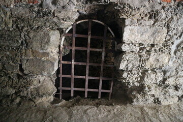 The barred window of the prison of ancient times. A window with a grill in a stone wall.