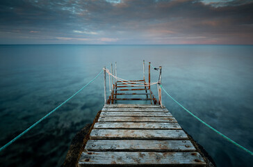 Naklejka premium Long wooden pier in the sea at sunset.