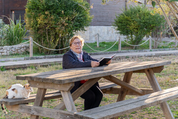 Fototapeta premium Older woman enjoying reading a book sitting on a bench in the park at sunset
