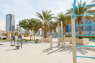 Outdoor sports ground with horizontal bars on a beach with palm trees and a cityscape with glass buildings on sunny day. Workout zone. Abu Dhabi, UAE
