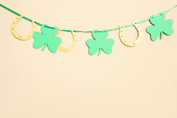 Garland with clovers and horseshoes hanging on beige wall at home. St. Patrick's Day celebration