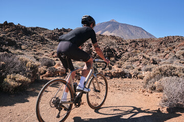 Cyclist practicing on gravel road. Fit man cyclist riding a gravel bike on gravel road with a view of the Teide volcano on Tenerife Canary Island,  Spain. Cycling gravel adventure. Effort mood.