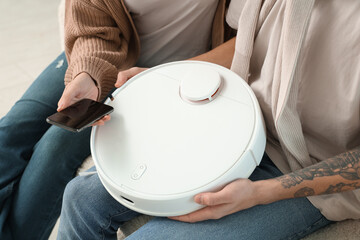 Young couple with modern robot vacuum cleaner and mobile phone in living room
