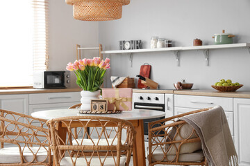 Calendar with date of International Women's Day, tulips and gift on dining table in kitchen